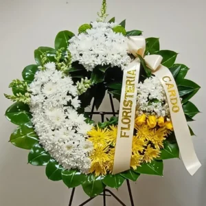 Corona fúnebre con crisantemos y margaritas blancas, detalles amarillos y rosas, arreglo floral elegante para condolencias.