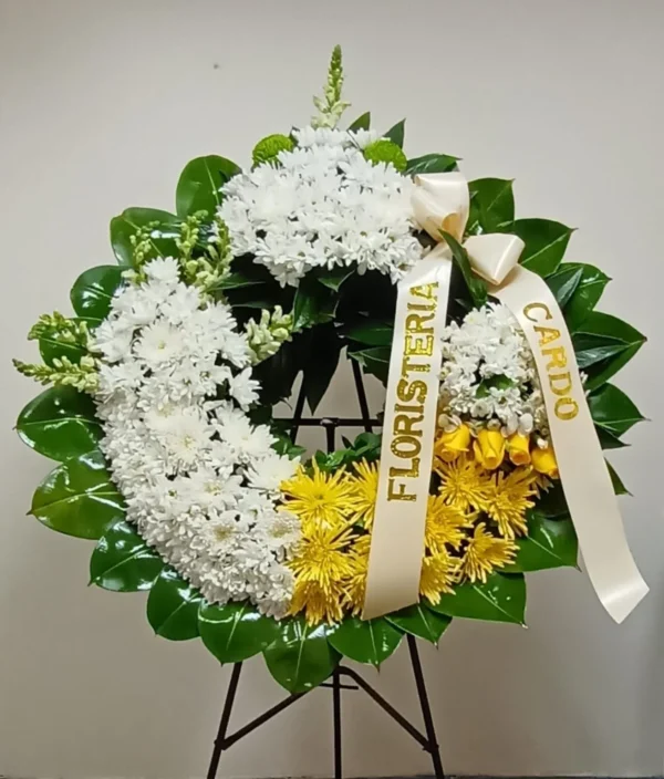 Corona fúnebre con crisantemos y margaritas blancas, detalles amarillos y rosas, arreglo floral elegante para condolencias.